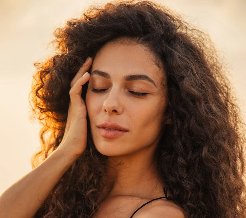 A woman with a clear, luminous complexion looking upward with a serene expression, framed by the soft-focus shadows of palm leaves against a neutral wall. - Profactional in Los Angeles, CA