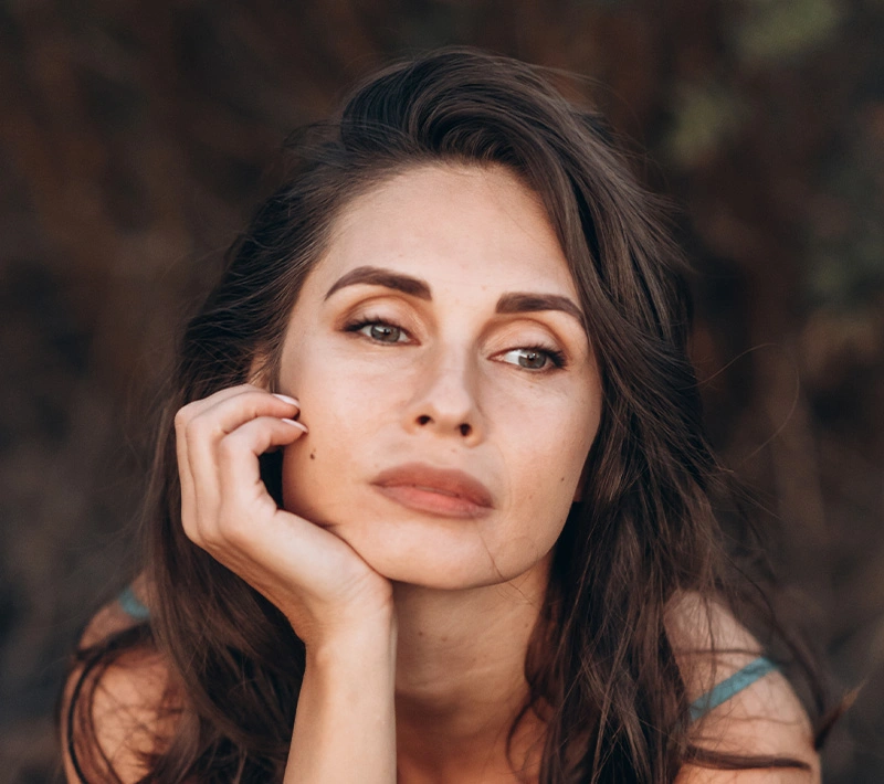 A portrait of a woman with a natural, clear complexion basking in bright sunlight, with the delicate shadows of palm leaves dancing across her face. - Sciton BBL heroic in Los Angeles, CA