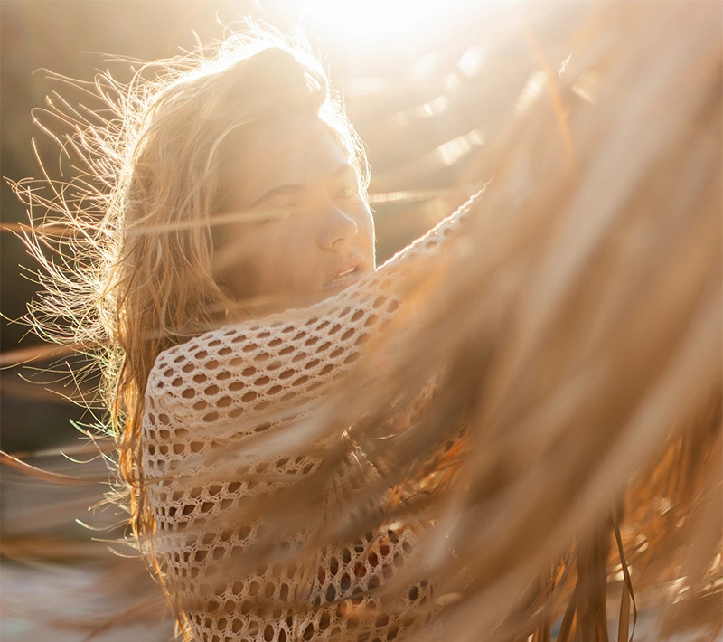 A woman with a clear, luminous complexion looking upward with a serene expression, framed by the soft-focus shadows of palm leaves. - Intro visible in Los Angeles, CA